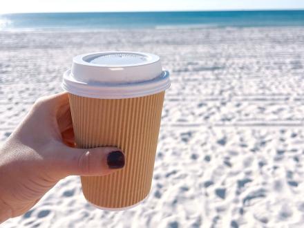 Hand holding a cup of coffee on the white-sand beaches of Gulf Shores