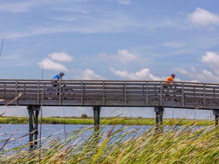 People biking over Lake Shelby along a boardwalk in Gulf State Park