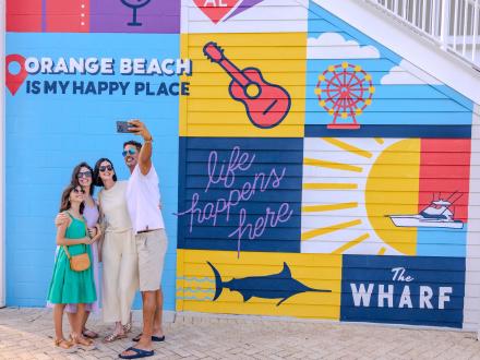 A family taking a selfie in front the mural at The Wharf